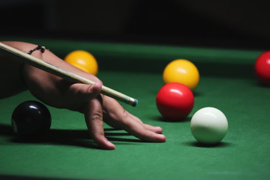 A close-up shot of a hand with a cue stick playing billiards on a green pool table.