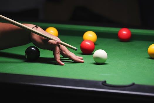 A close-up shot of a hand positioning a cue stick on a billiard table with colorful balls.