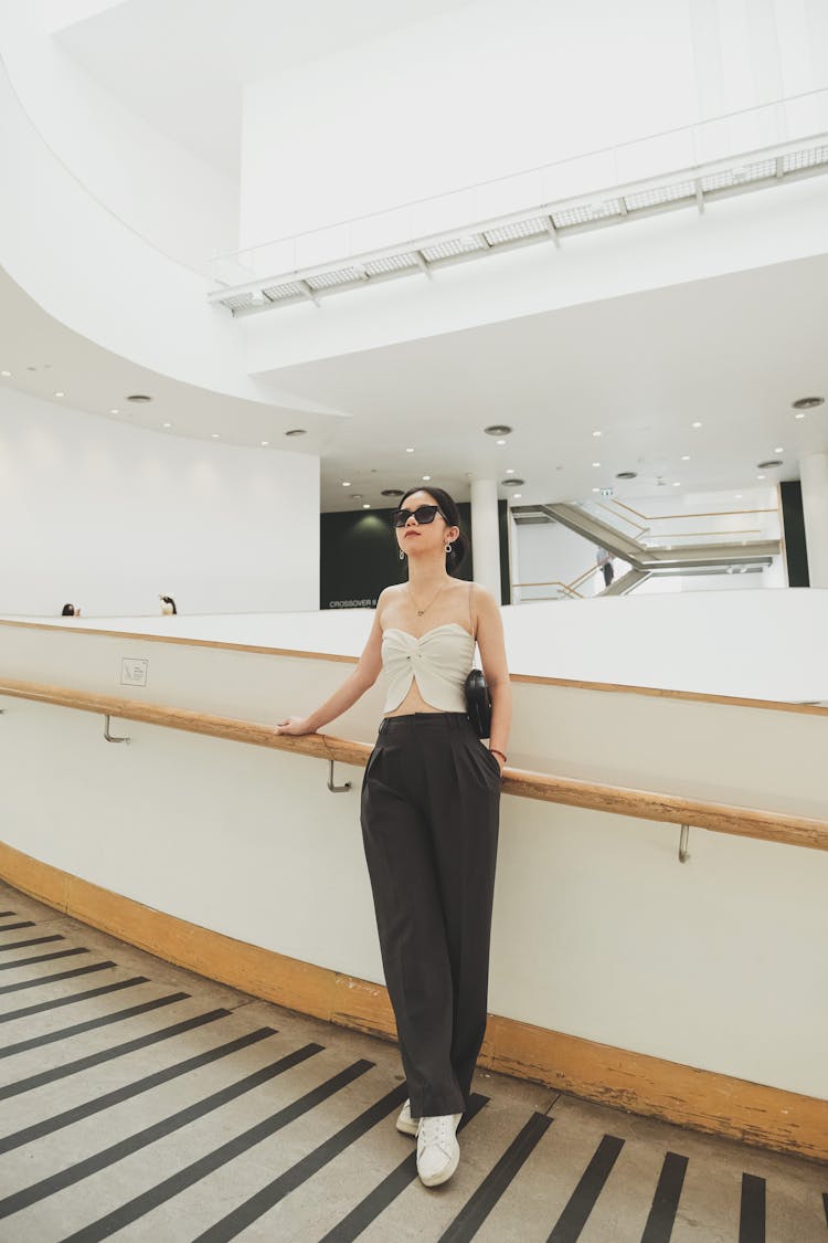 A Woman In A White Tube Top And Black Pants Leaning On A Handrail