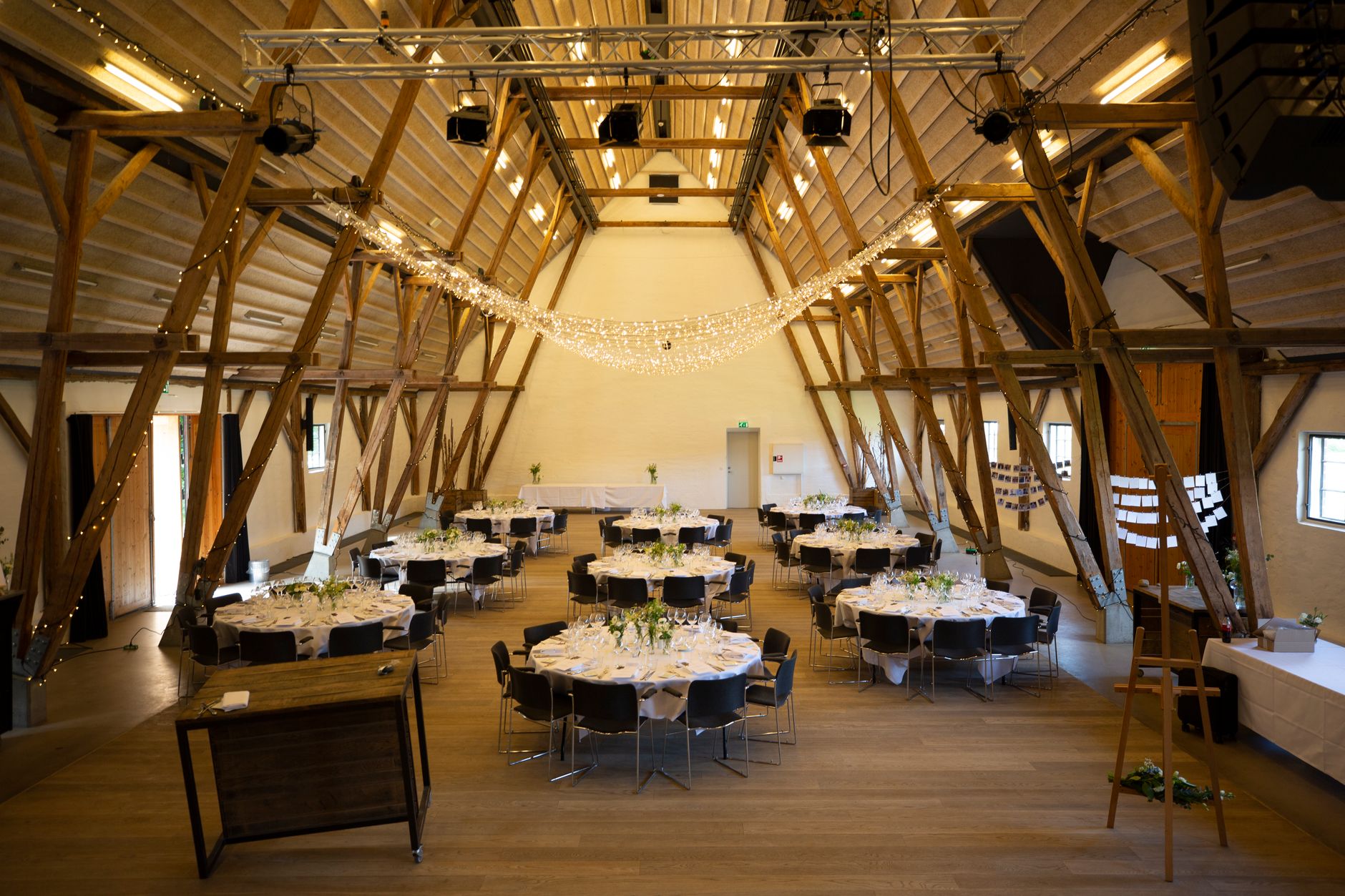 Spacious banquet hall with round tables and rustic wooden beams, ready for an event.