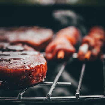 Sizzling meat on a charcoal grill with a rich, juicy glaze in a close-up shot.