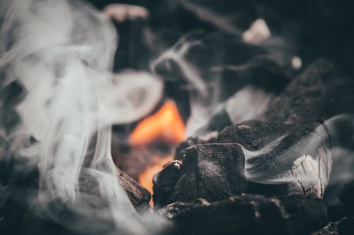 Free A close-up view of burning charcoal emitting flames and smoke, creating a warm and dramatic atmosphere. Stock Photo