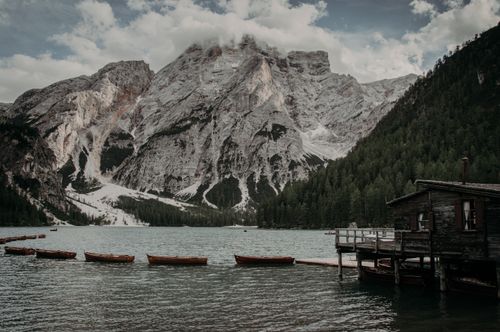 Free Serene lake view with rustic boats and towering mountain backdrop, perfect for nature lovers. Stock Photo