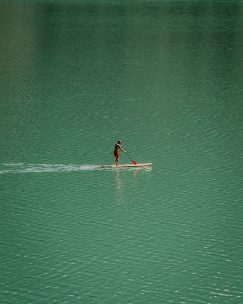 Free Man paddleboards on a serene turquoise lake, creating ripples in the calm water. Stock Photo