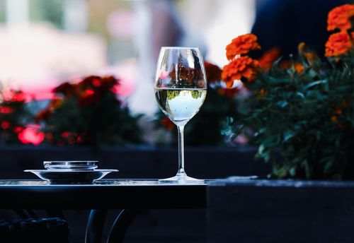 Free A wine glass on a table surrounded by colorful flowers, capturing a serene outdoor cafe scene. Stock Photo