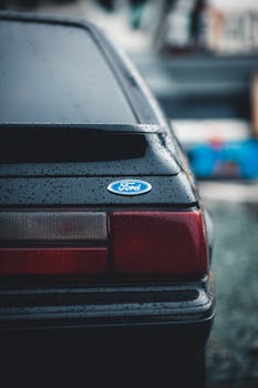 A detailed look at the rain-covered rear of a Ford car, showcasing its logo.