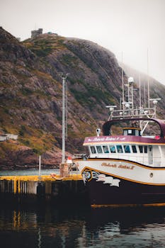 A fishing boat docked at a pier with rugged cliffs in the background, offering a serene coastal view.