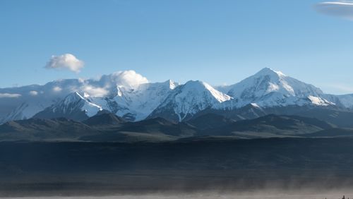 Free Snow-covered Denali mountains in Alaska, featuring clear blue skies and misty valleys. Stock Photo