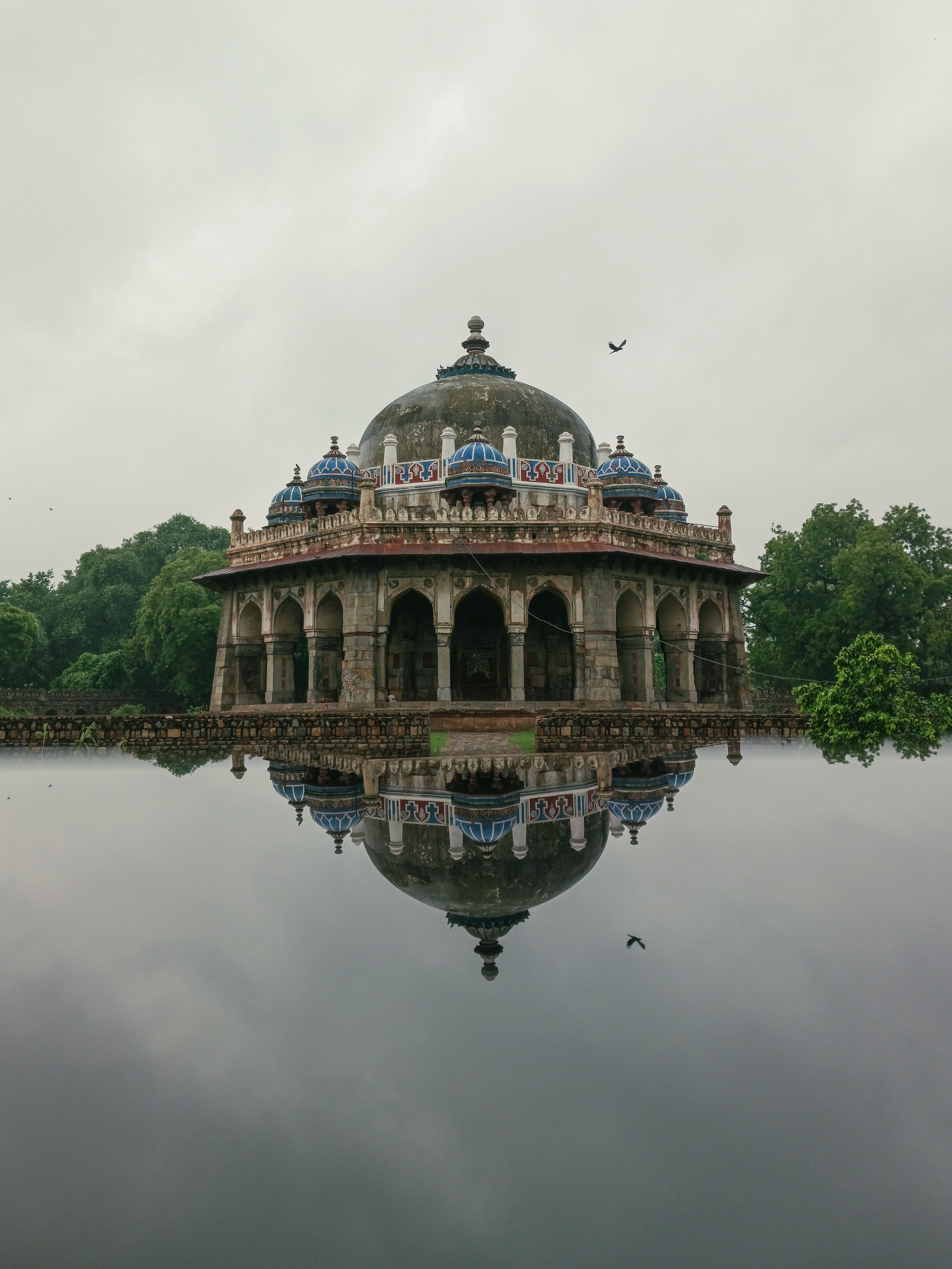 A stunning reflection of Isa Khan's Tomb in Delhi amidst tranquil waters, highlighting Mughal architecture.