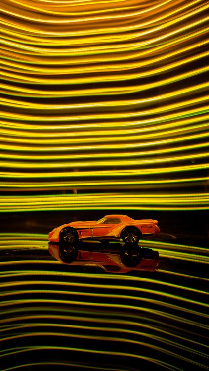 Free Miniature toy car against vibrant neon LED backdrop with reflective surface. Stock Photo