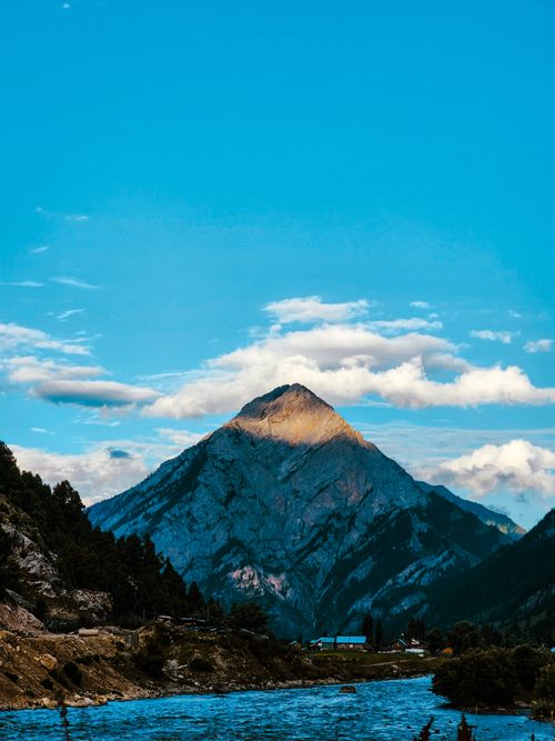 Free Scenic mountain landscape with a serene river, under a vibrant blue sky with white clouds. Stock Photo