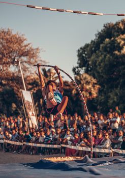 Dynamic shot of a teenage athlete performing a pole vault in front of an audience during a sunset competition.