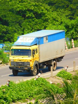 Colorful truck drives on a sunny Chattogram road, surrounded by greenery.