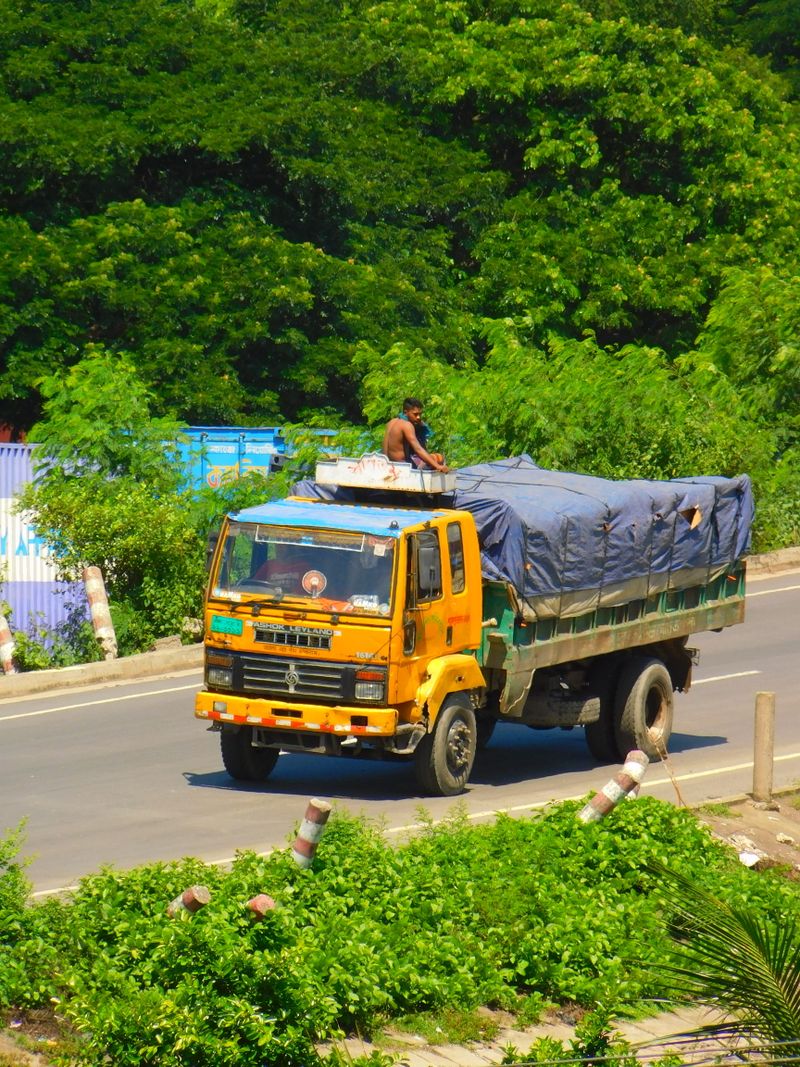 Driver standing on a yellow dropside truck bed