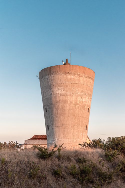 Free A tall concrete water tower stands against a clear blue sky in a rural setting. Stock Photo