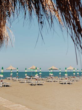 Tranquil beach with umbrellas and sun loungers in Tale, Albania, under clear blue skies.