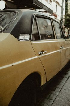 Close-up of a vintage yellow car parked on a city street, showcasing classic design.