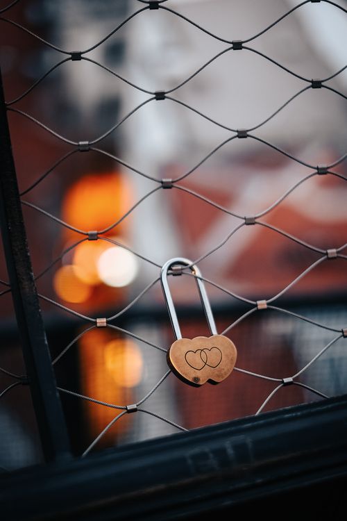 Free Heart-shaped padlock hangs on a fence with blurred bokeh background. Stock Photo