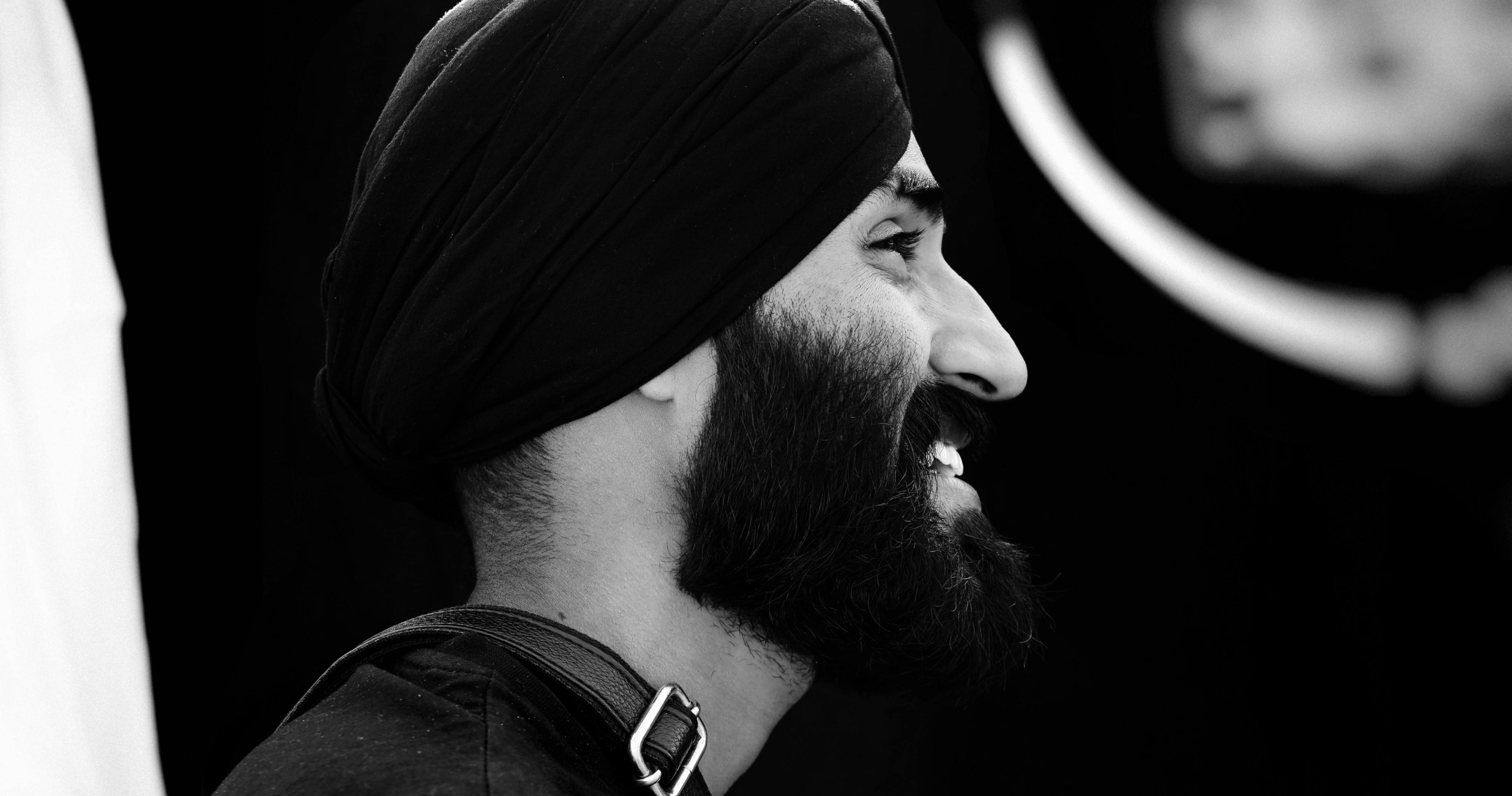 Monochrome side profile of a man with beard and turban smiling.