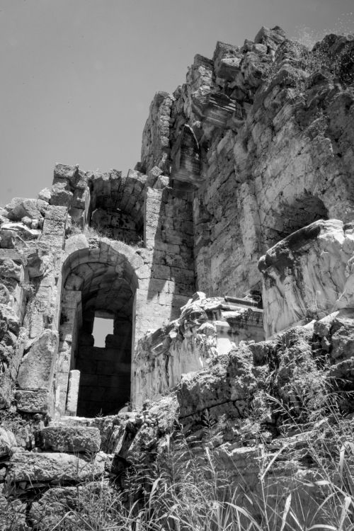 Free Black and white image of ancient stone ruins under a bright sky with grasses in foreground. Stock Photo