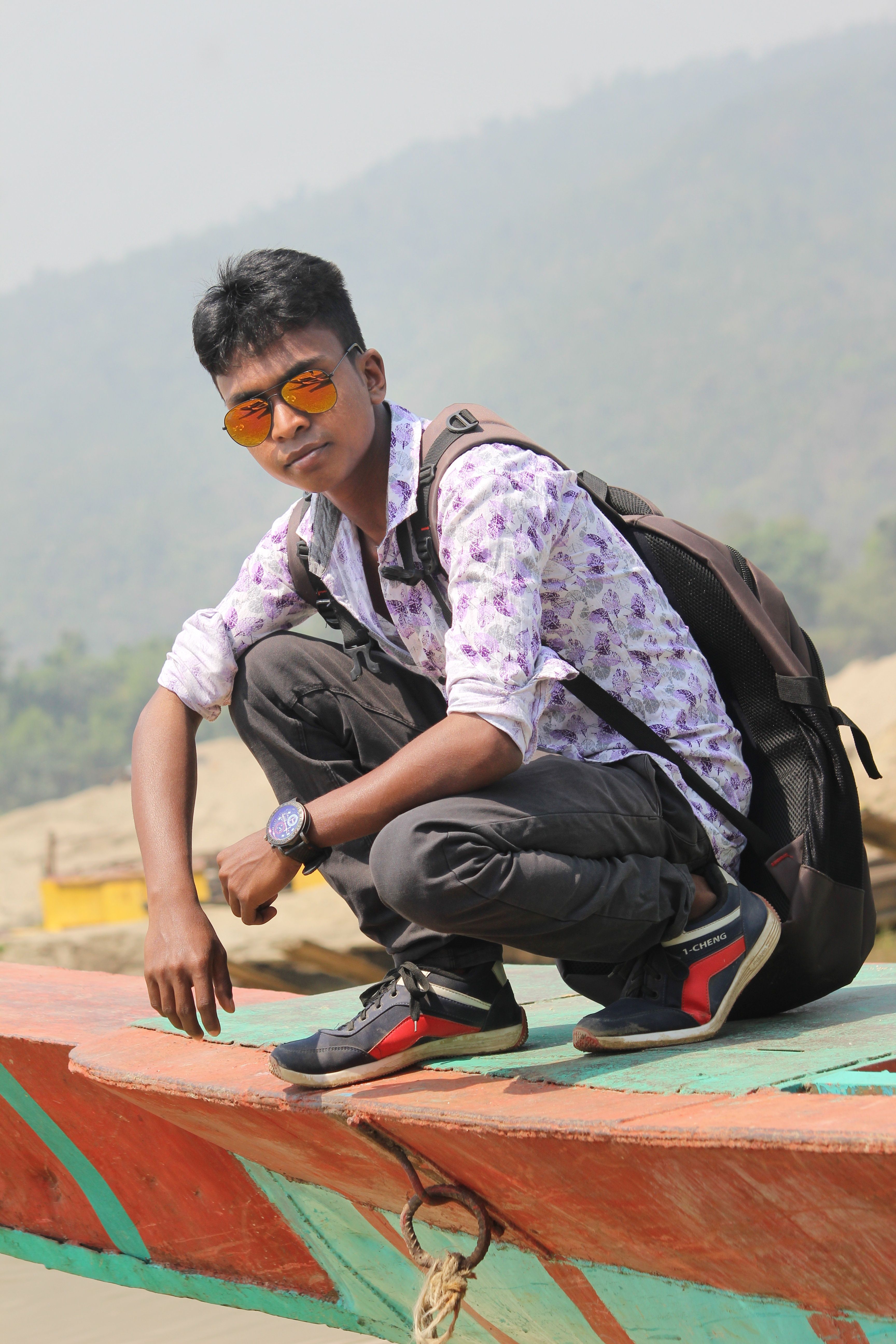 A young man in sunglasses poses with a backpack on a boat in Jaflong, Bangladesh.