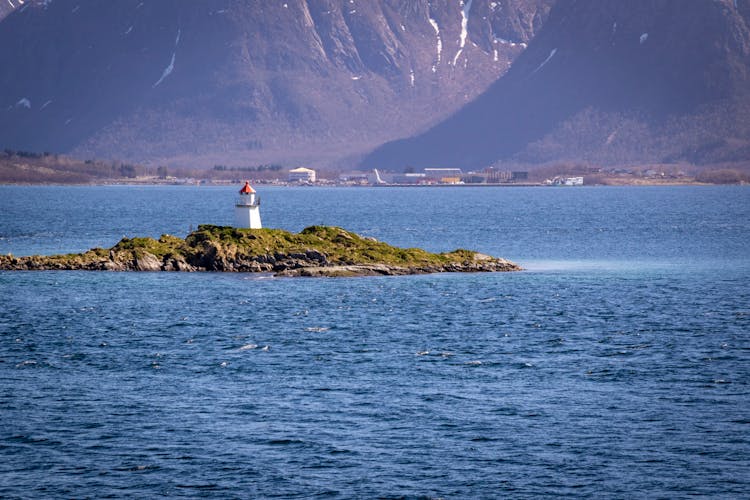 Small White Lighthouse On A Rocky Islet In A Norwegian Fjord