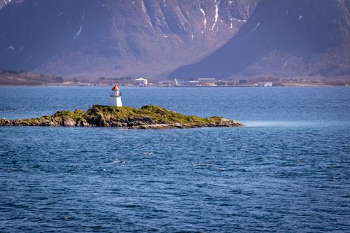 Free A picturesque lighthouse on a small Norwegian islet surrounded by mountain views and a seascape. Stock Photo