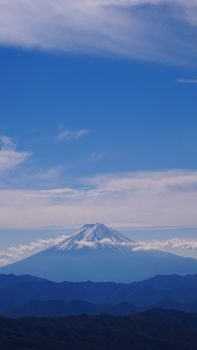 A breathtaking aerial view of a snow-covered mountain peak beneath a vivid blue sky with clouds.