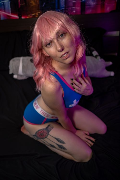 Free Woman with pink hair and tattoo posing on bed in colorful lighting. Stock Photo