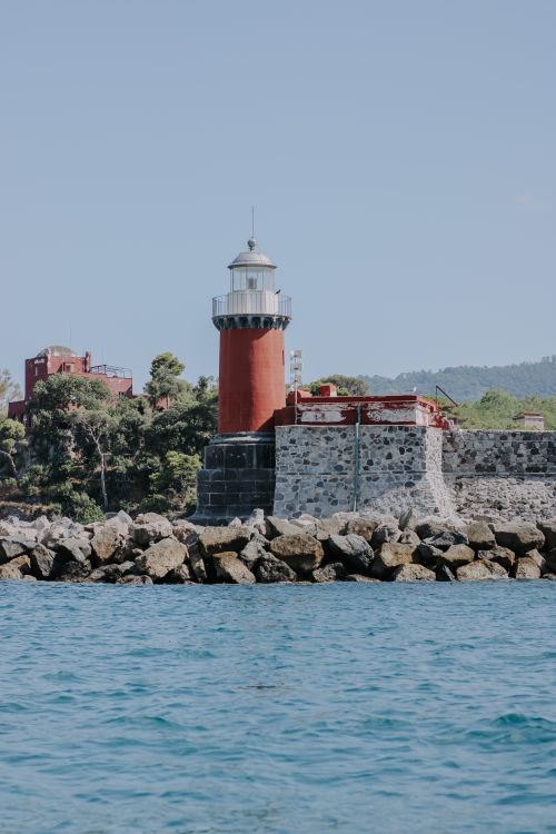 Free Picturesque lighthouse standing on a rocky coastline under a clear sky. Stock Photo