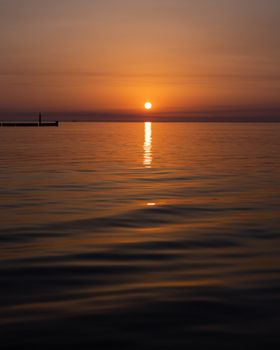 Peaceful sunset over calm waters in Graal-Müritz, Germany, with a silhouette on the horizon.