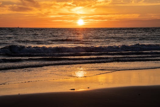 Capture the serene beauty of a sunset over the ocean with waves gently kissing the sandy shore.