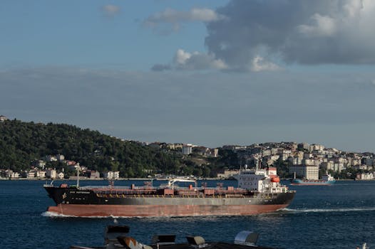 Cargo ship sailing through the Bosporus in Istanbul with cityscape and hills in the background.