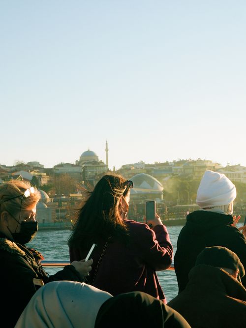 Free Tourists on a ferry taking photos of Istanbul's iconic Bosphorus and skyline, featuring Ottoman architecture. Stock Photo