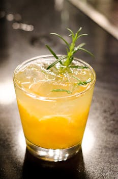 Vibrant citrus cocktail with ice and a green herb garnish, captured indoors.