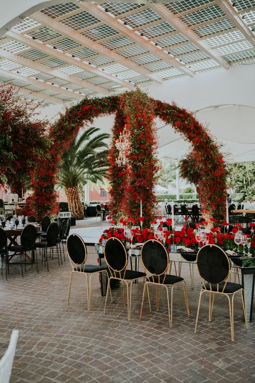 Free Lush outdoor wedding setup featuring vibrant red floral arches and elegant table settings. Stock Photo