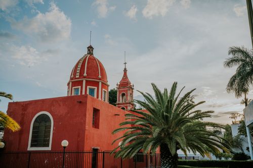 Free Charming red church with dome and palm trees under a serene sky, showcasing architectural elegance. Stock Photo