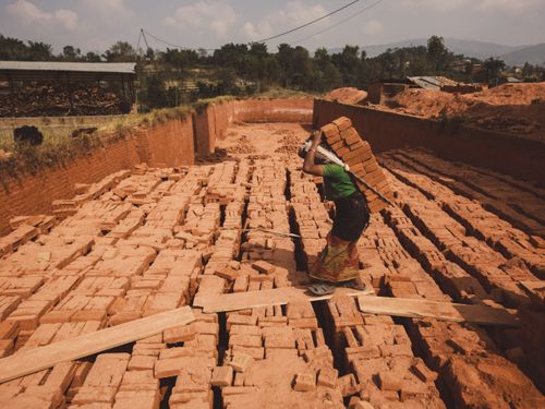 Free A woman working and carrying multiple bricks in an outdoor brick factory. Stock Photo