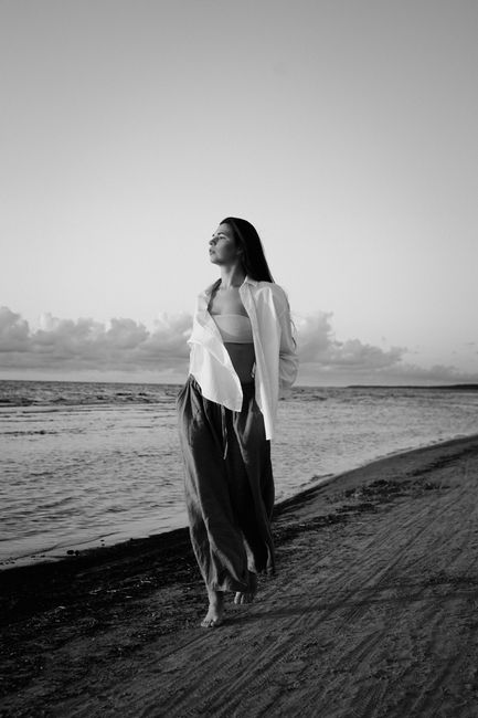 A woman strolls along Kalngale beach in a serene black and white setting.