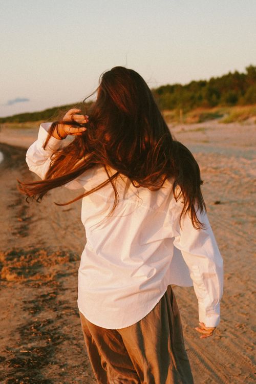 Free Woman with long hair walking on Kalngale beach, Latvia, in a white shirt during a windy summer evening. Stock Photo