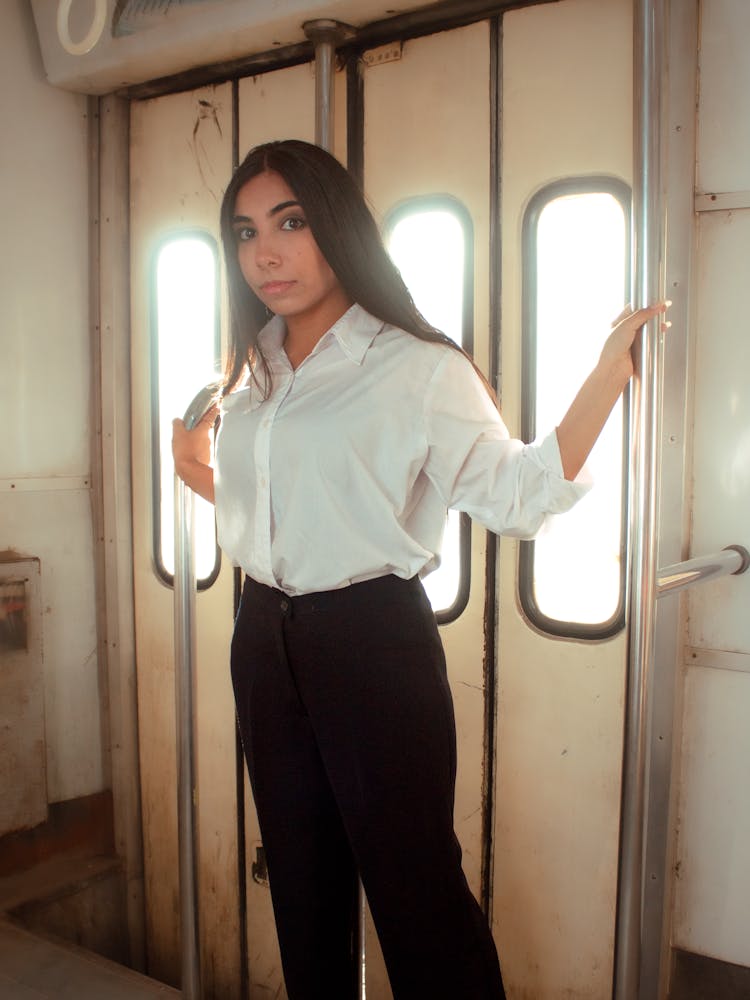 A Woman In White Long Sleeves Holding On Metal Bars Inside The Train