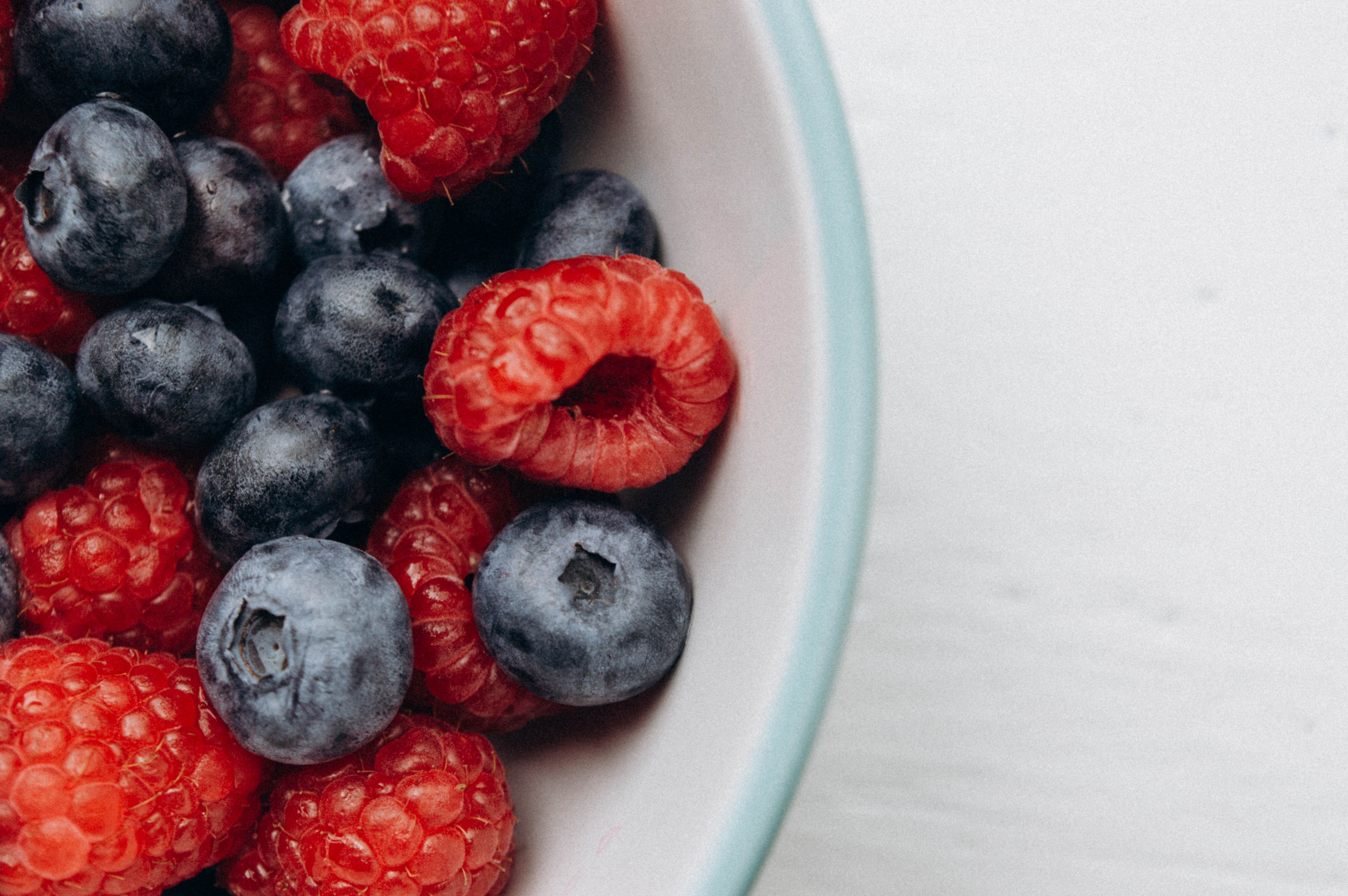 Close-up of fresh blueberries and raspberries in a white bowl, offering a vibrant mix of colors.