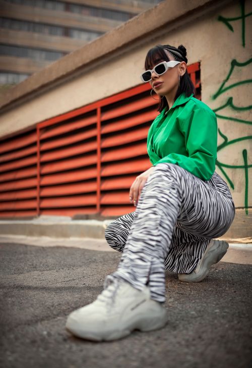 Free Fashionable woman crouching outside in zebra print pants and green top, exuding urban style. Stock Photo
