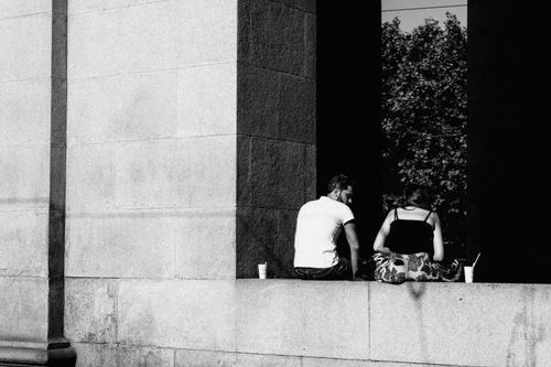 Free A couple sits together on a concrete ledge outdoors in a black and white setting, facing away. Stock Photo