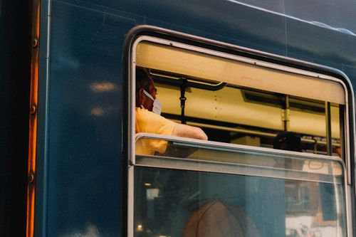 Free A man wearing a face mask looks out the window of a train, embodying modern public transportation. Stock Photo