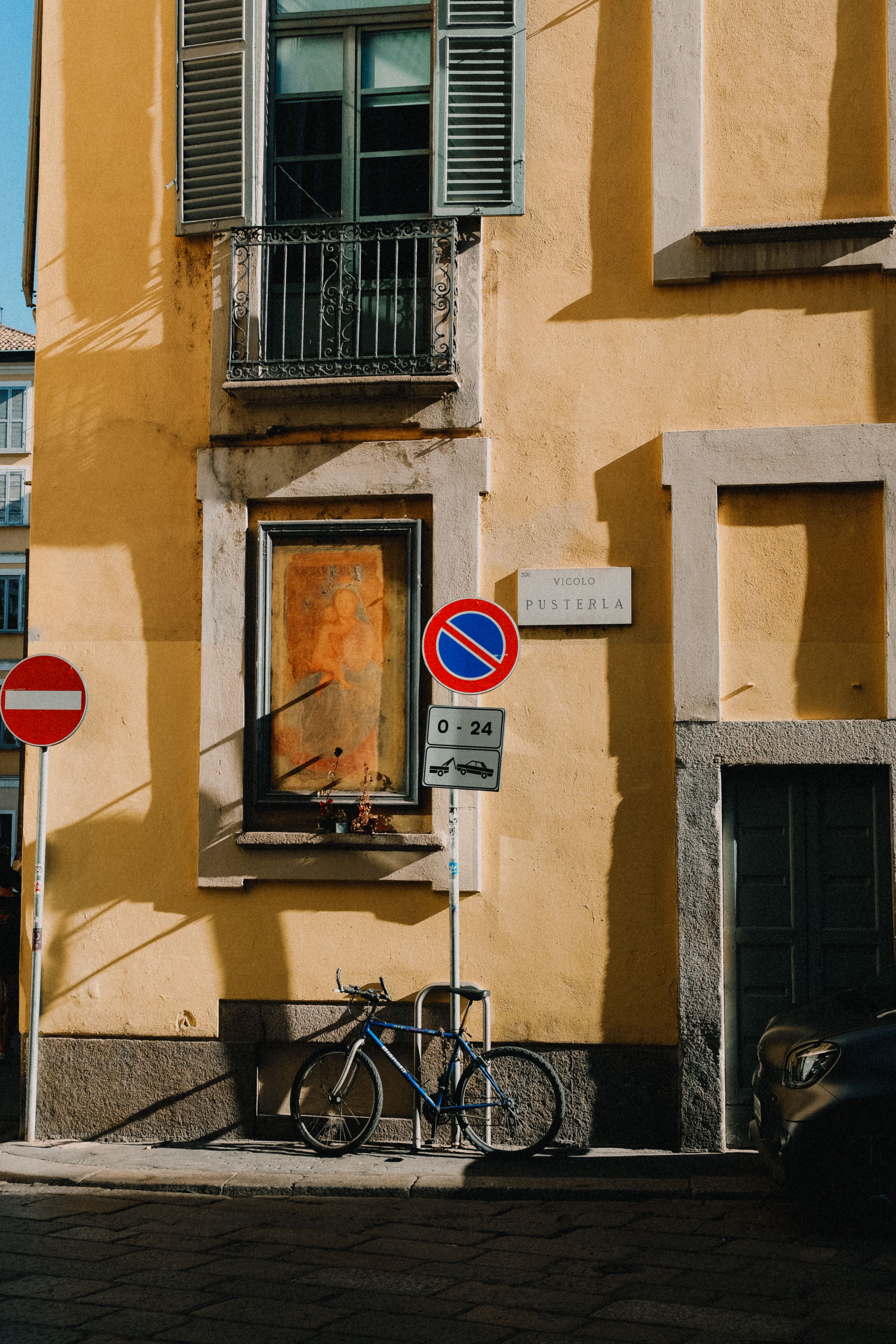 Bicycle parked beside an old yellow building with traffic signs on a sunny day.