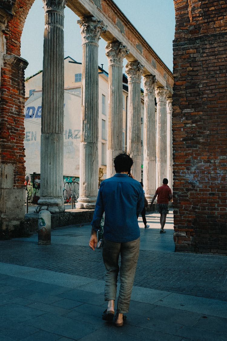 A Man In A Blue Shirt In A Phone Call While Walking At The Colonne Di San Lorenzo In Milan