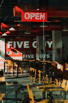 Sunlit Five Guys interior featuring empty tables and chairs, highlighting the restaurant's open sign.
