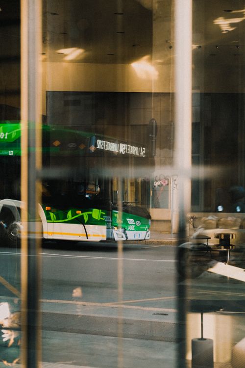 Free A city bus reflected on a glass window with urban street scene. Stock Photo