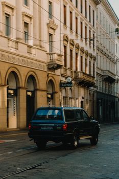 A classic SUV drives down an old town street lined with historic buildings, evoking urban charm.